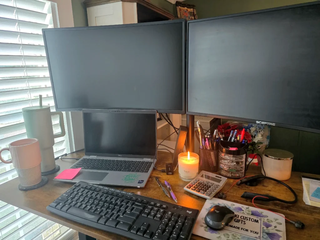 A calm workspace with a closed laptop, black screens, a burning candle, coffee cup, water bottle, calculator, and a bright pink sticky note.